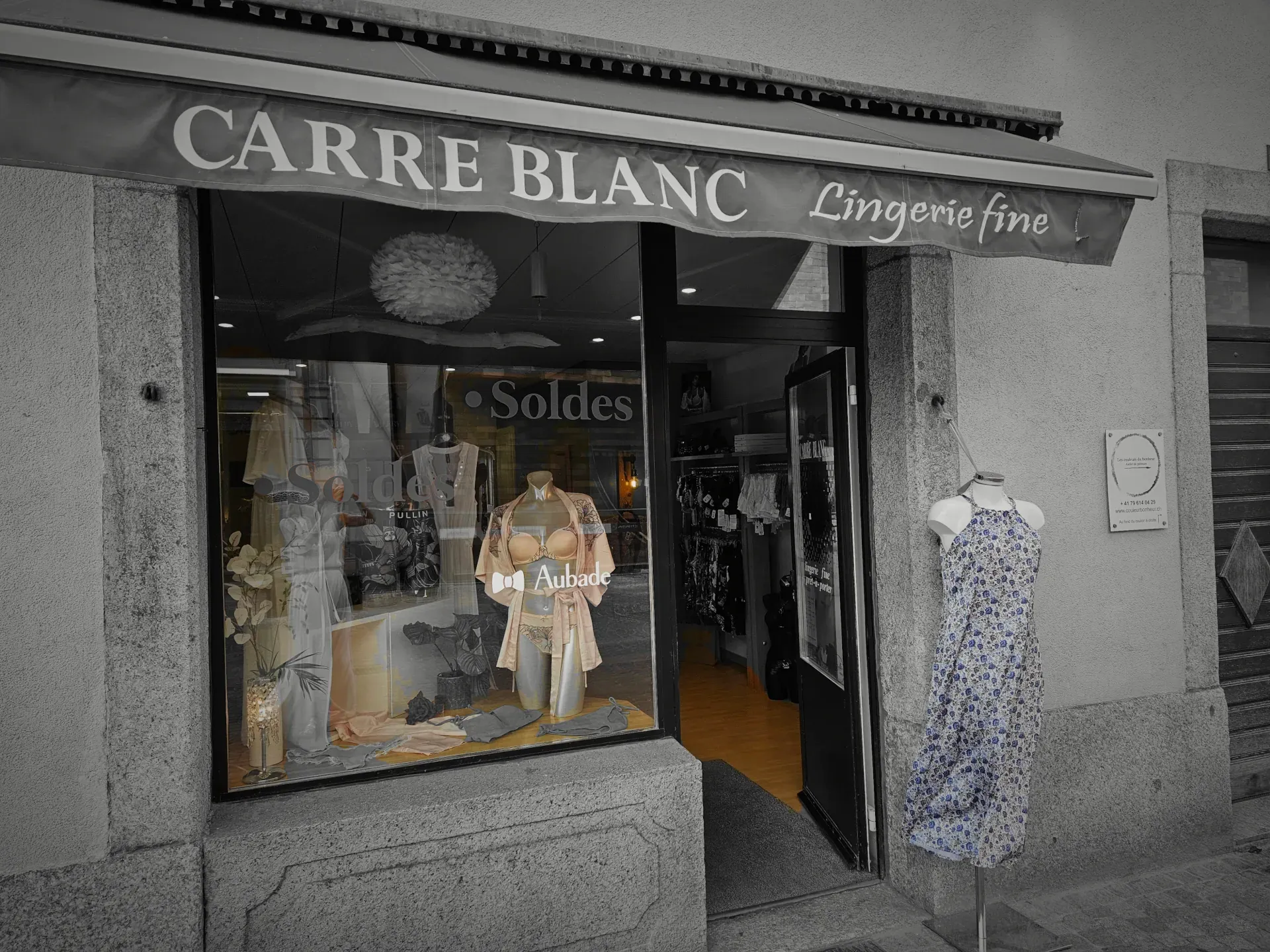 Charmante petite boutique à la vitrine savamment décorée Vitrine de la boutique Carré Blanc dans une rue pavée avec des mannequins portant de la lingerie ou des maillots de bain